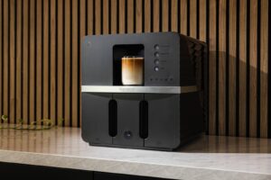 Black Bronson automatic coffee machine with a latte on a stone kitchen counter