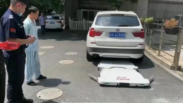Flat car-moving robot unfolded behind a white SUV as a security guard and a hospital patient look on