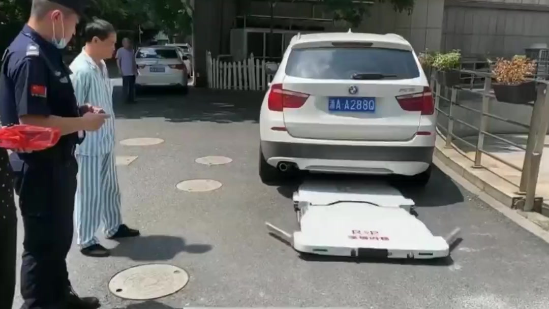 Flat car-moving robot unfolded behind a white SUV as a security guard and a hospital patient look on