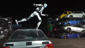 Unitree H2-X humanoid robot leaping off the roof of a silver car in a junkyard at night