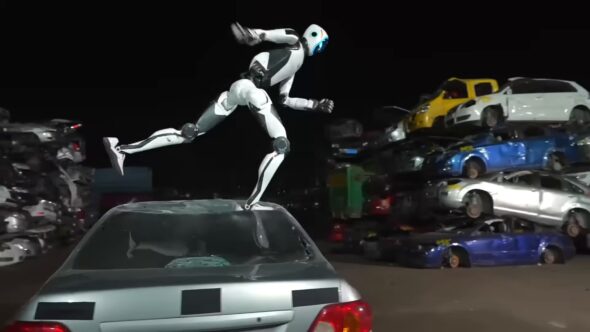 Unitree H2-X humanoid robot leaping off the roof of a silver car in a junkyard at night