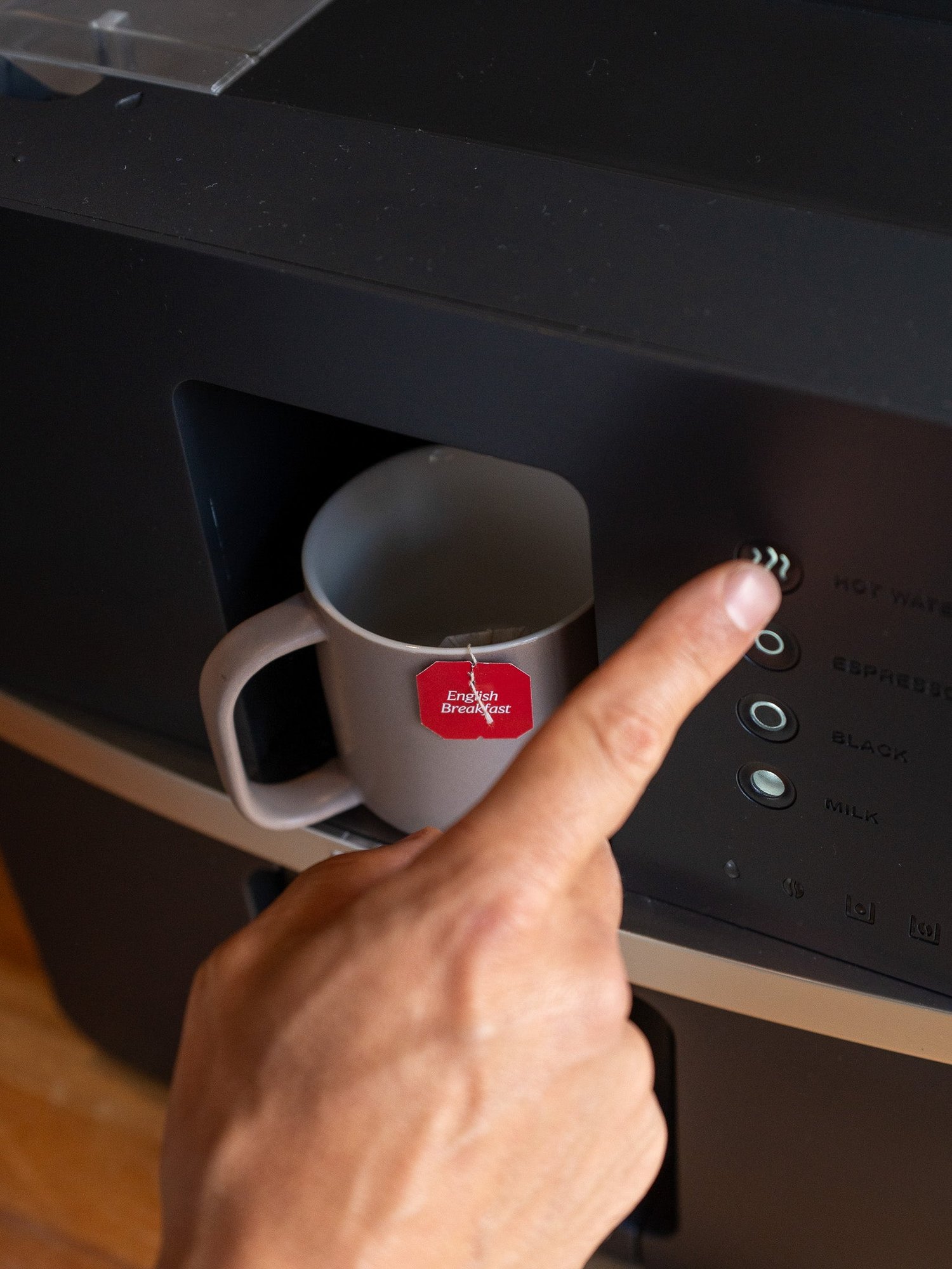 Finger pressing a glowing button on the Bronson coffee machine with a mug inside