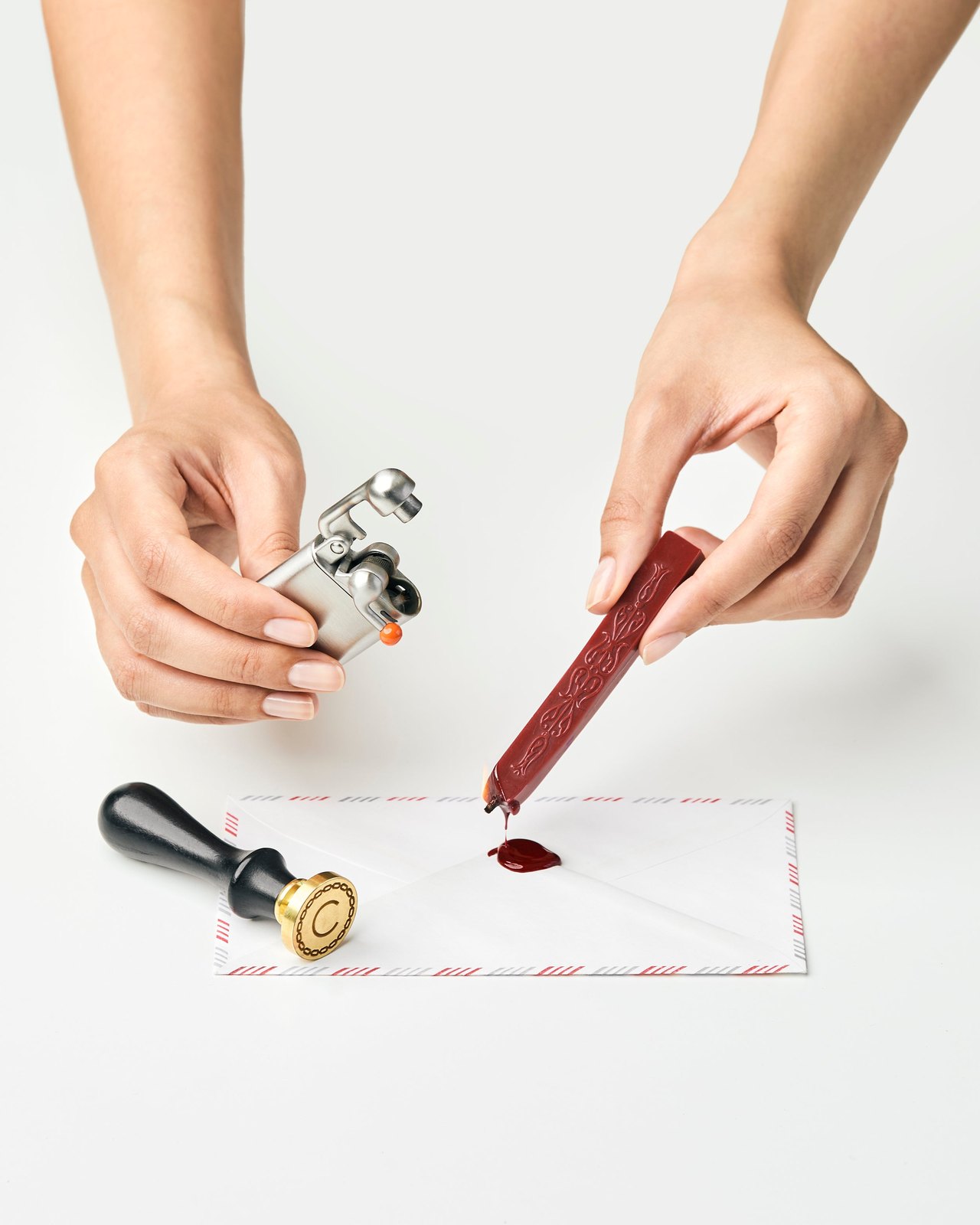 Hands melting red sealing wax onto an envelope next to a brass seal stamp