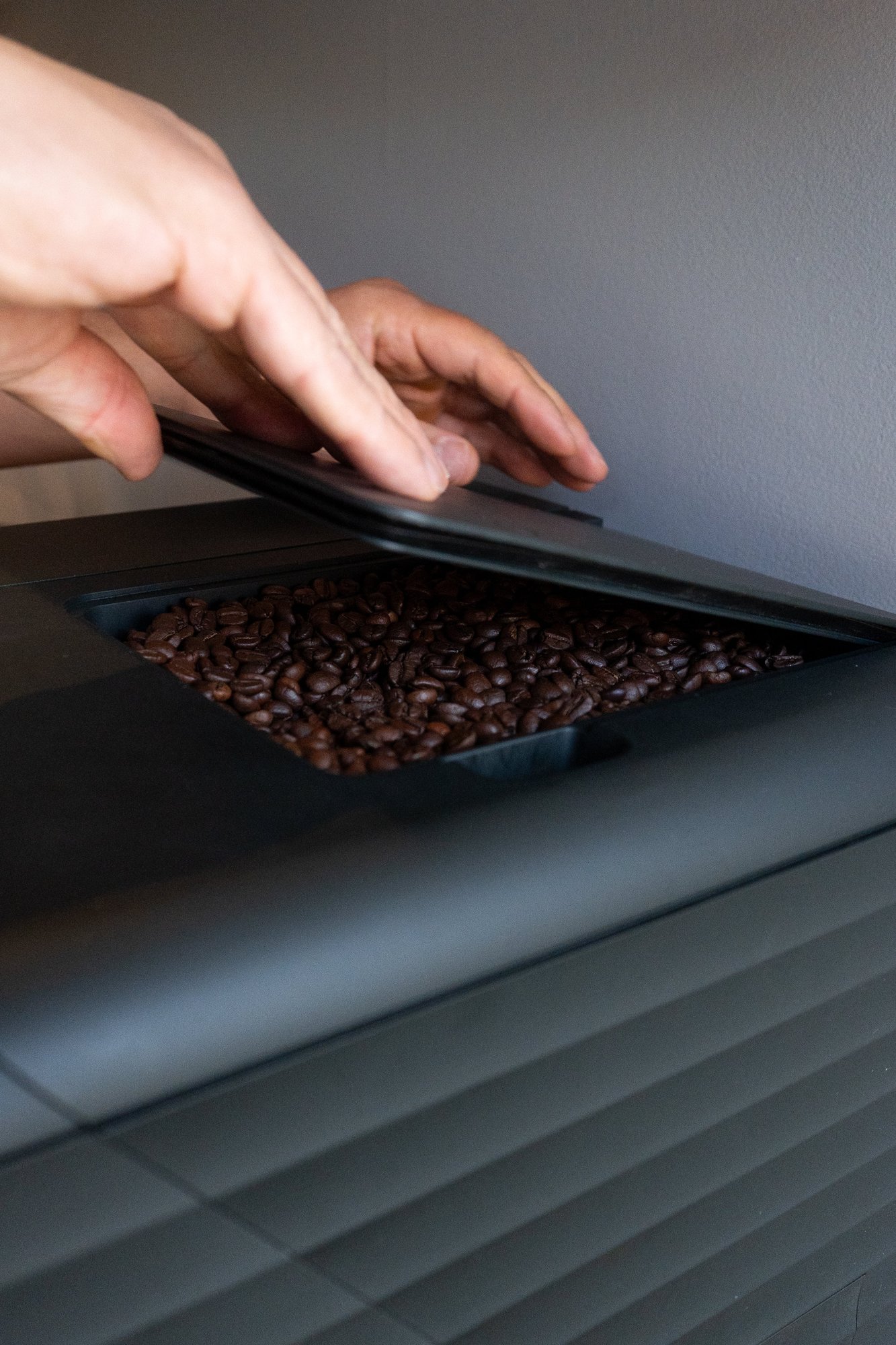 Hand opening the Bronson bean hopper lid to show whole coffee beans