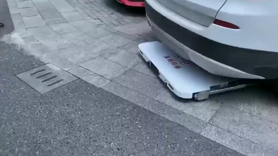 Car-moving robot carrying a white SUV across the pavement into a parking spot