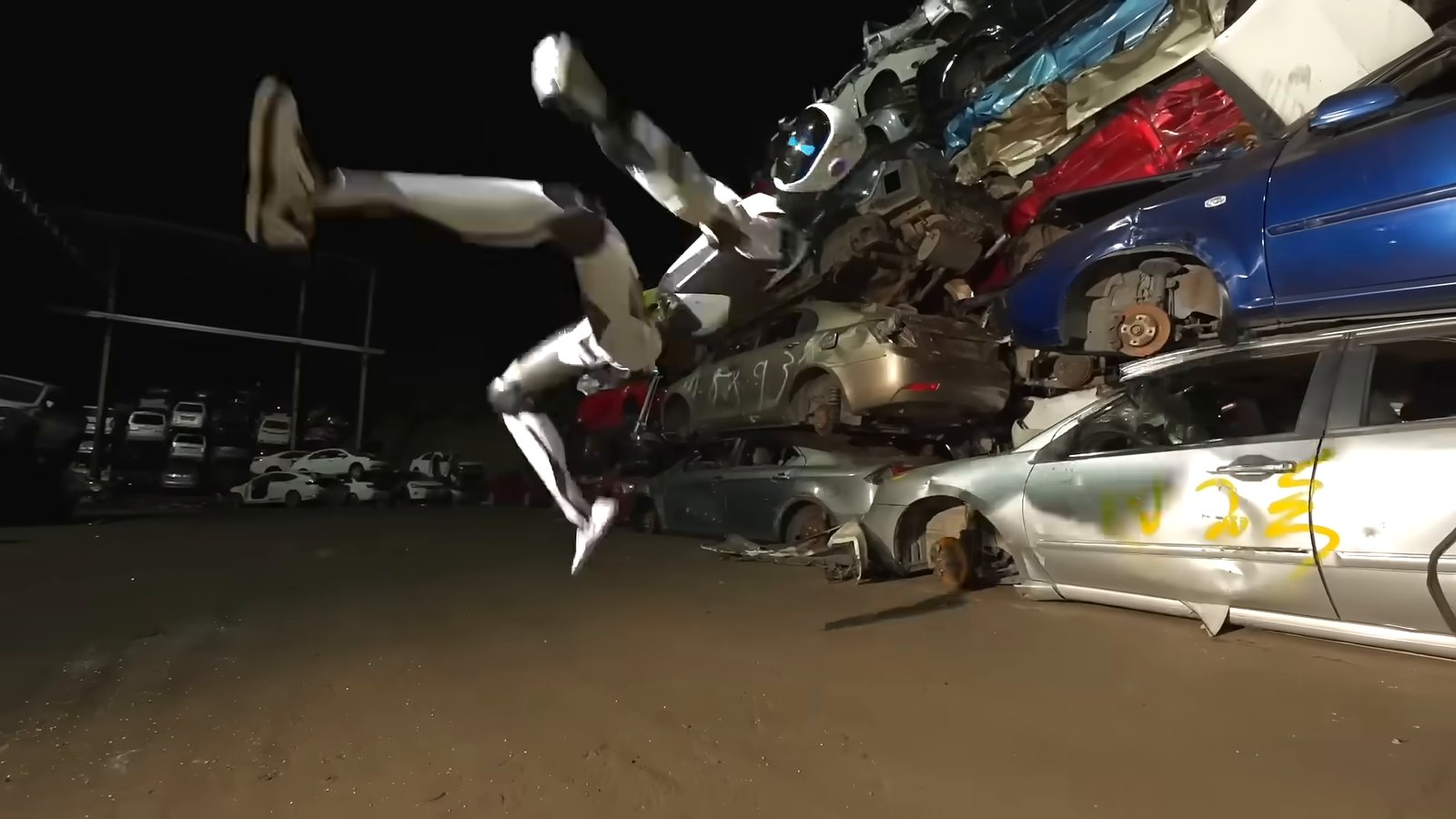 Unitree H2-X robot throwing a flying kick at a stack of crushed cars