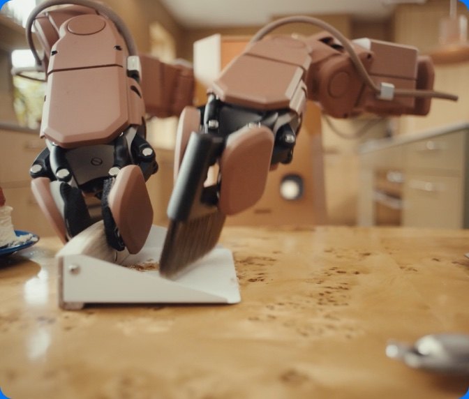 Voxel robot grippers sweeping crumbs into a dustpan on a kitchen counter
