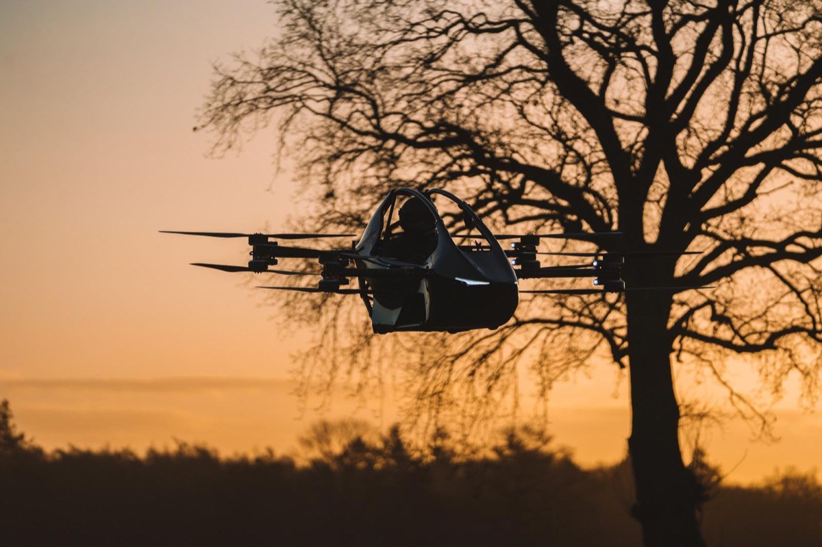 YIVTOL S-Zero flying past a bare tree against an orange sunset sky