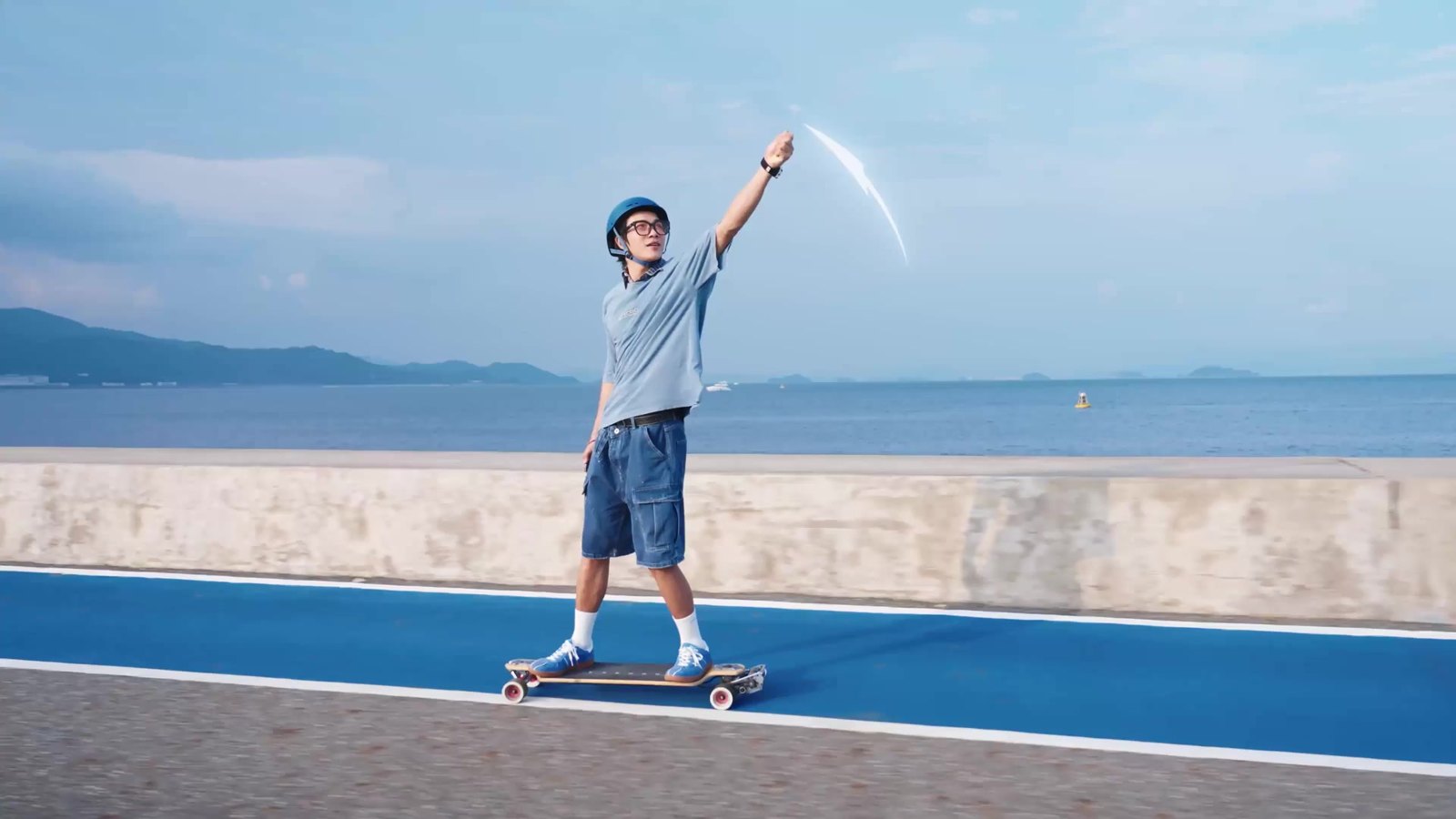 Skateboarder waving up at the Antigravity A1 drone filming from overhead on a seaside path