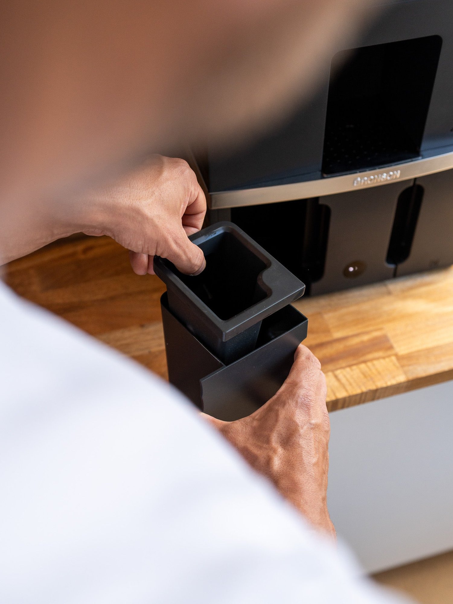 Hand pulling a removable waste container out of the Bronson coffee machine