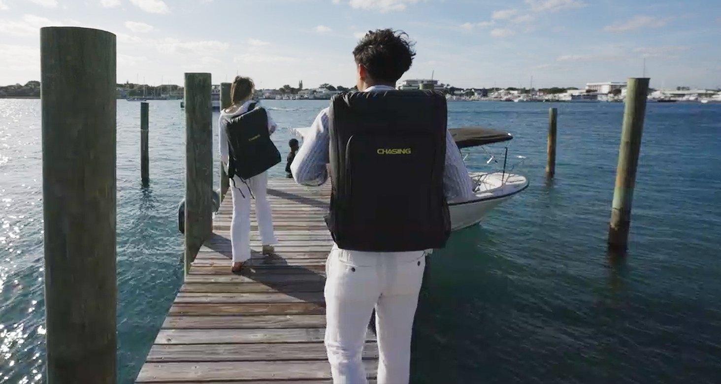 Two people walking down a wooden dock carrying CHASING underwater drone backpacks toward a boat