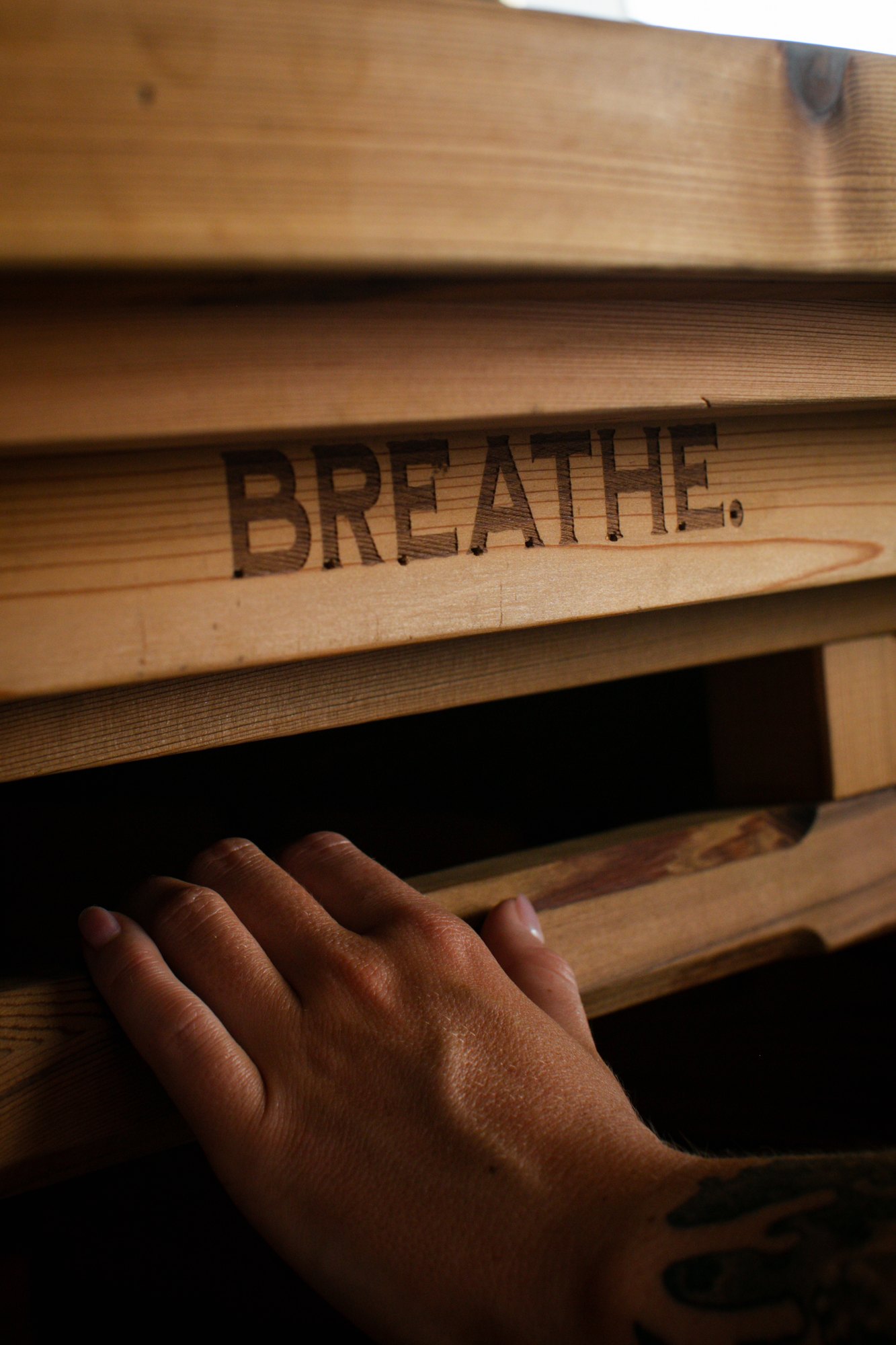 Hand sliding open The Hot Box Sauna lid with BREATHE engraved in the cedar