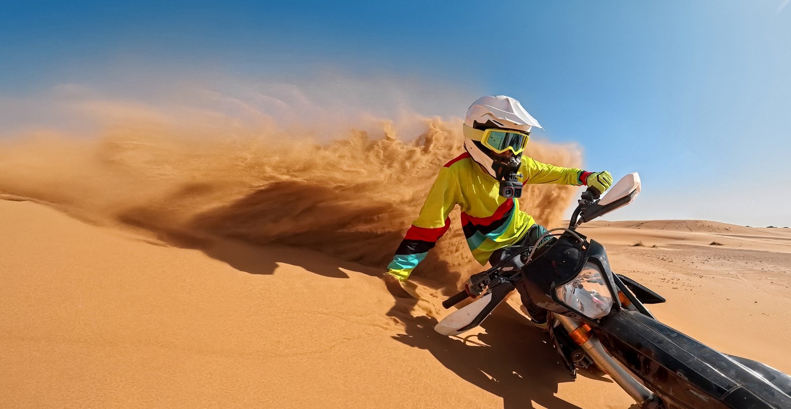 Sample shot from the Insta360 Ace Pro 2 of a dirt bike rider kicking up a wave of sand on a desert dune
