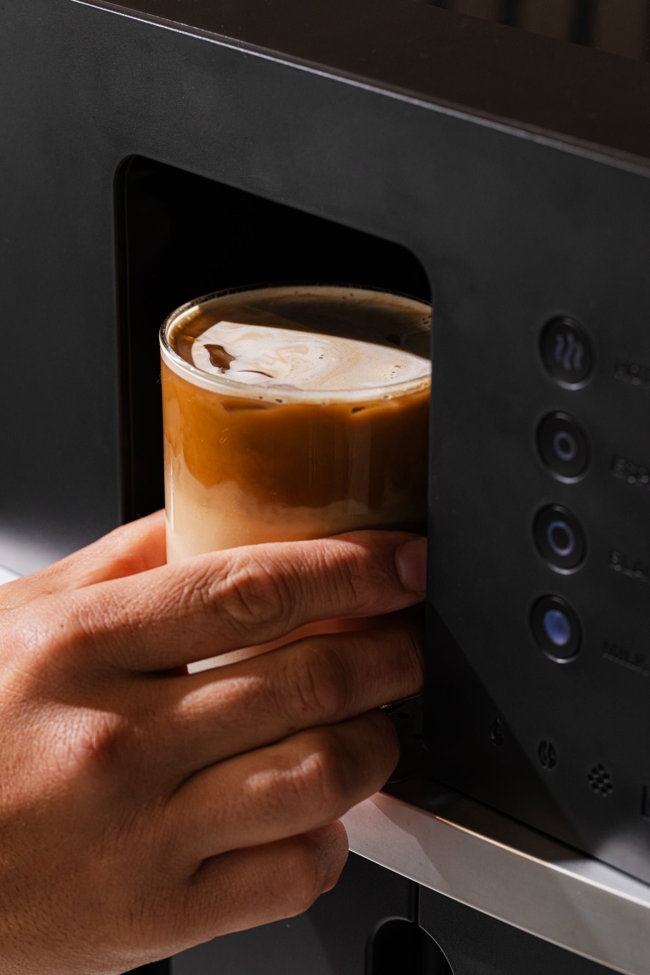 Hand taking an iced latte out of the Bronson coffee machine