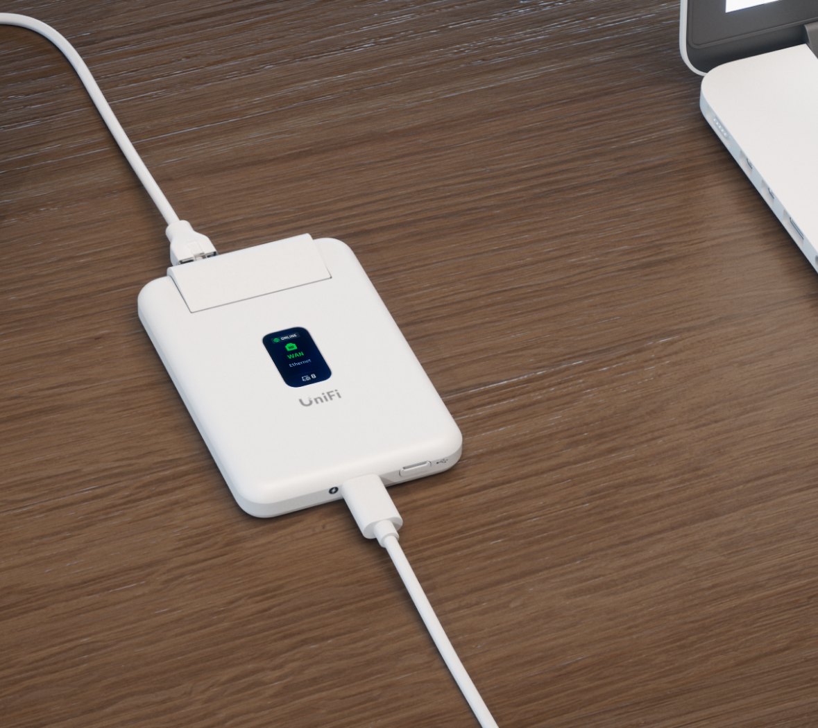 UniFi Travel Router lying on a wooden desk powered by a white USB-C cable