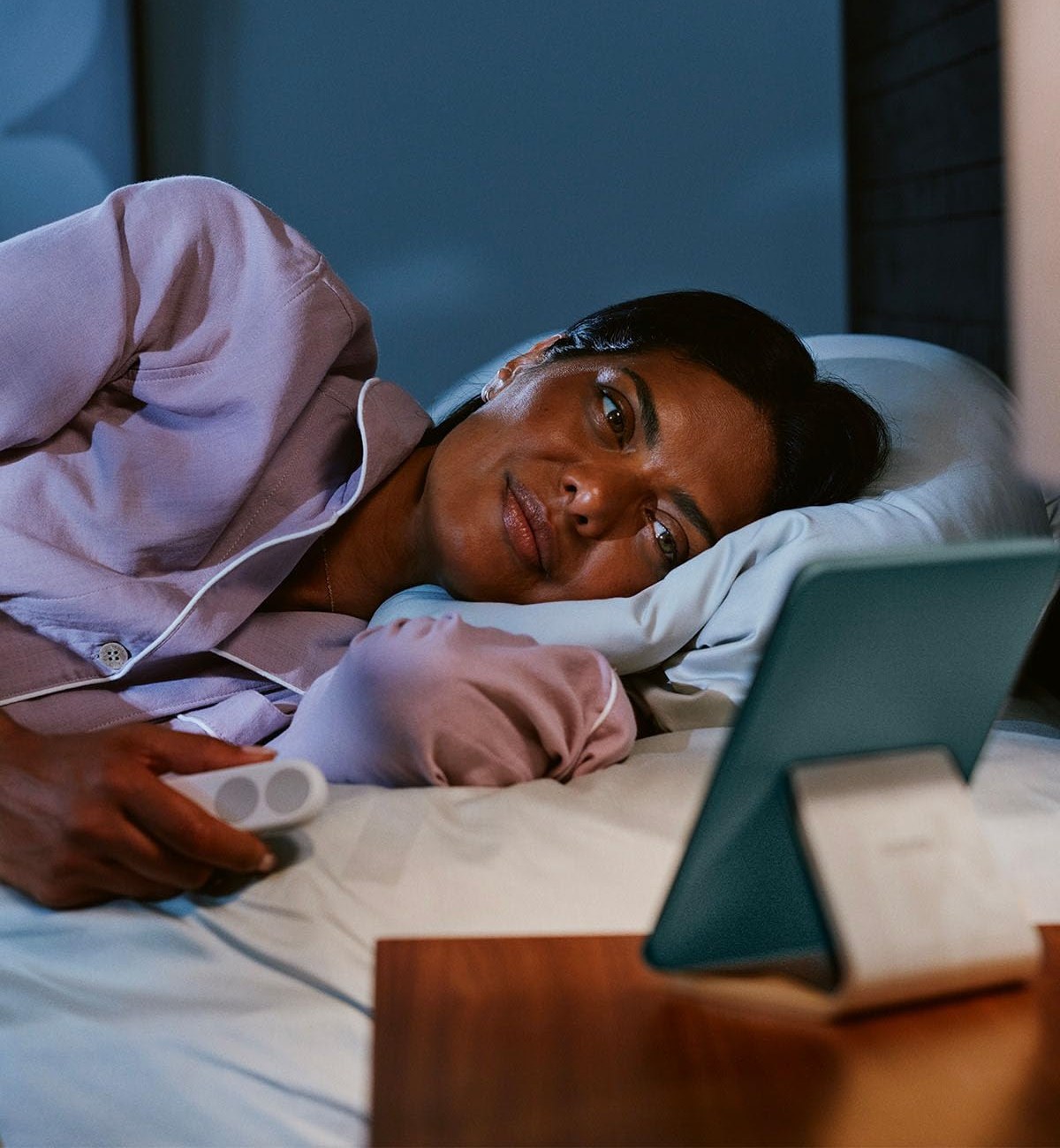 Woman reading in bed with the Kindle Click remote in hand and her Kindle propped on a stand